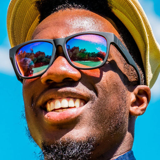 Fit and style showcase of large black sunglasses with rose-tinted, high contrast lenses. Display of men's fit on a golf course.