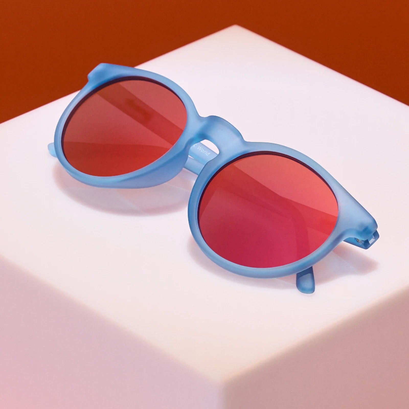 Product showcase of dusty blue circle-shaped sunglasses with red reflective lenses. 